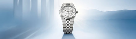 A silver Rolex wristwatch with a patterned dial displayed against a soft blue, light-filled background.