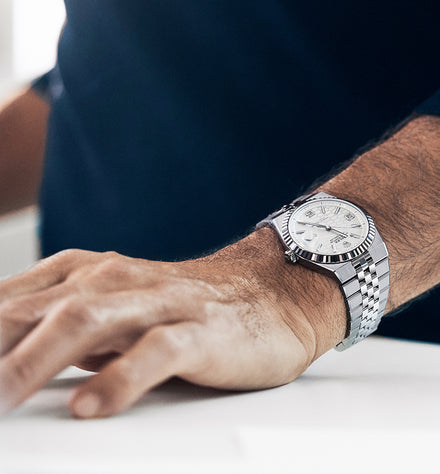 A close-up of a mans wrist wearing a silver luxury watch with a metal band.
