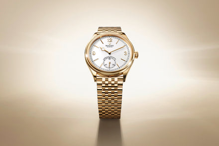 A gold Rolex wristwatch with a white dial displayed against a soft beige gradient background.