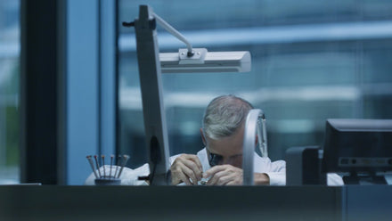 A person examines an object closely at a desk, using a magnifying tool, in a modern office setting.