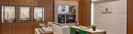 Modern Rolex showroom with wooden walls, display cases of watches, and branded signage on a tiled wall.
