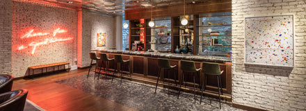 Modern bar with marble countertop, velvet stools, exposed brick walls, neon sign, and colorful artwork.