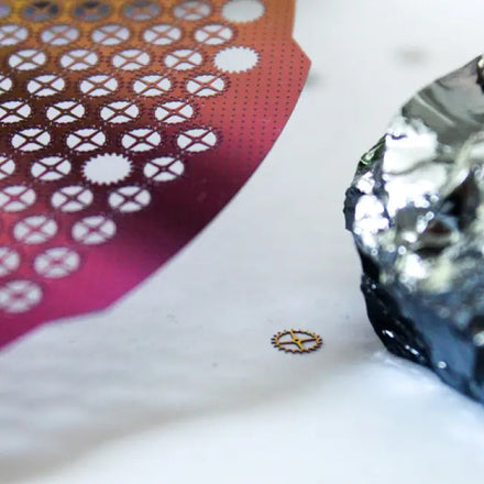 Close-up of a patterned pink wafer with circular cut-outs next to a crumpled piece of silver foil.
