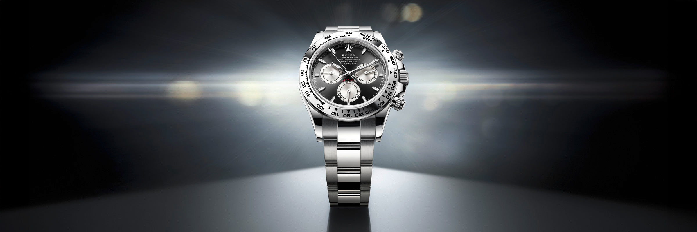 A silver luxury wristwatch with a black dial and three subdials, spotlighted against a dark background.