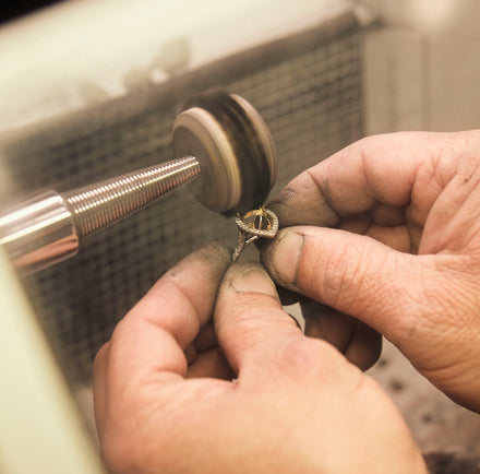 Hands polishing a ring with a rotary tool, close-up view in a workshop setting.