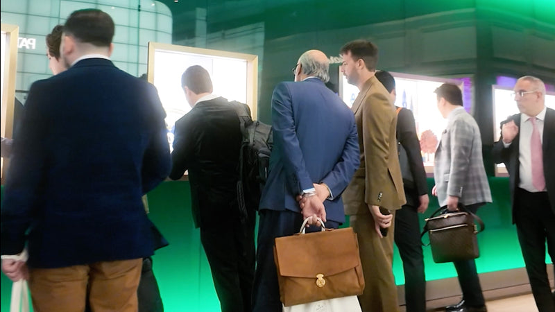 Several men in business attire stand in line at a brightly lit counter with green decor, carrying briefcases.