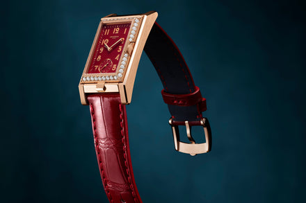 Luxury watch with red face and strap on a dark blue background