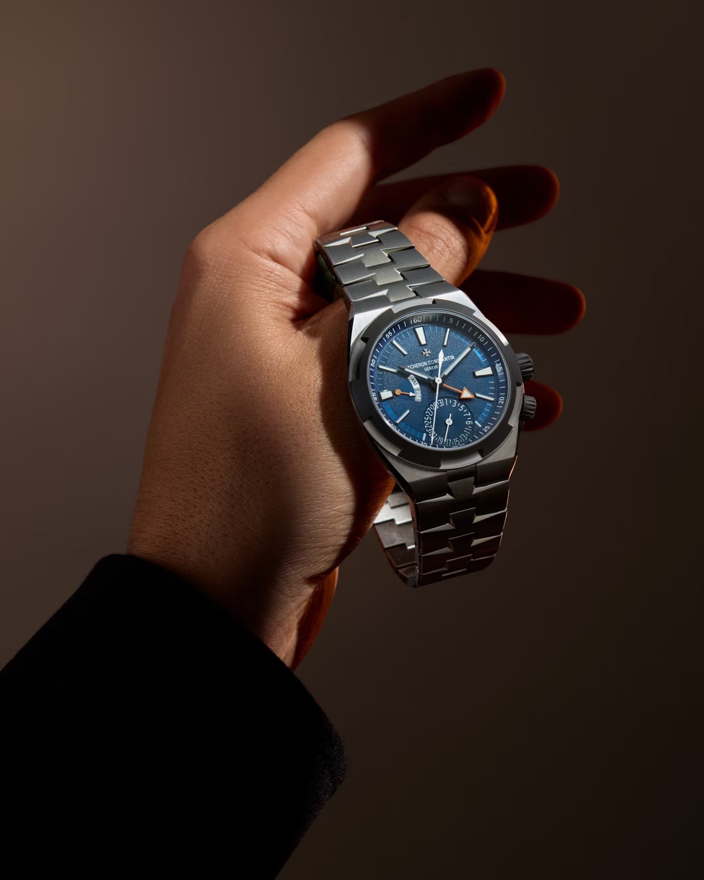 Stainless steel watch with blue dial, dual time subdials, and metal bracelet held in hand.