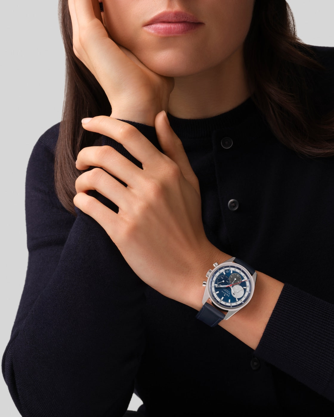 Woman in a black top rests her face on her hand, showcasing the Zenith Chronomaster Original—a striking blue and silver wristwatch.