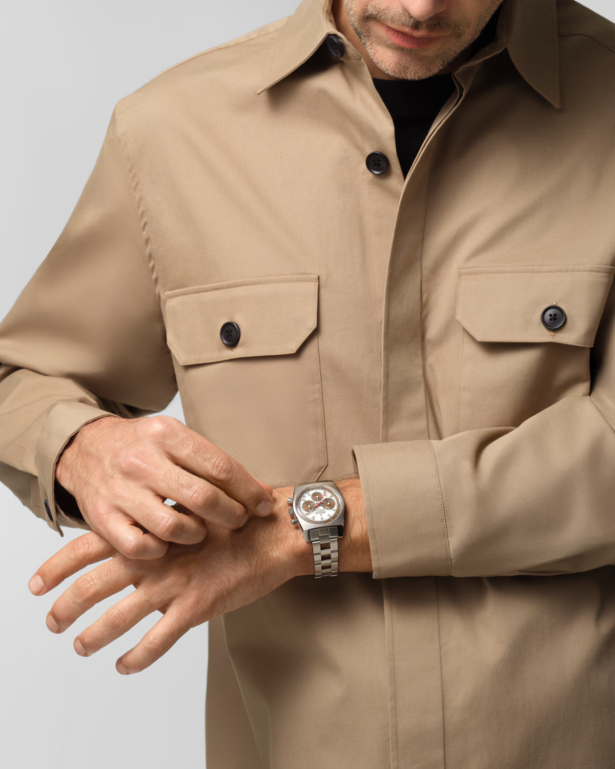 Man wearing a beige jacket and a watch on a light gray background