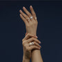 Two hands with manicured nails, each adorned with Chopards Ice Cube diamond ring and other gold and silver rings, are crossed against a dark background, showcasing minimalist elegance and a modern aesthetic.