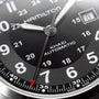 Close-up of a Hamilton Khaki Field Auto watch face in black, featuring numerals, hands, a date window at 8, and a red-tipped second hand, powered by the H-10 automatic caliber with impressive power reserve.