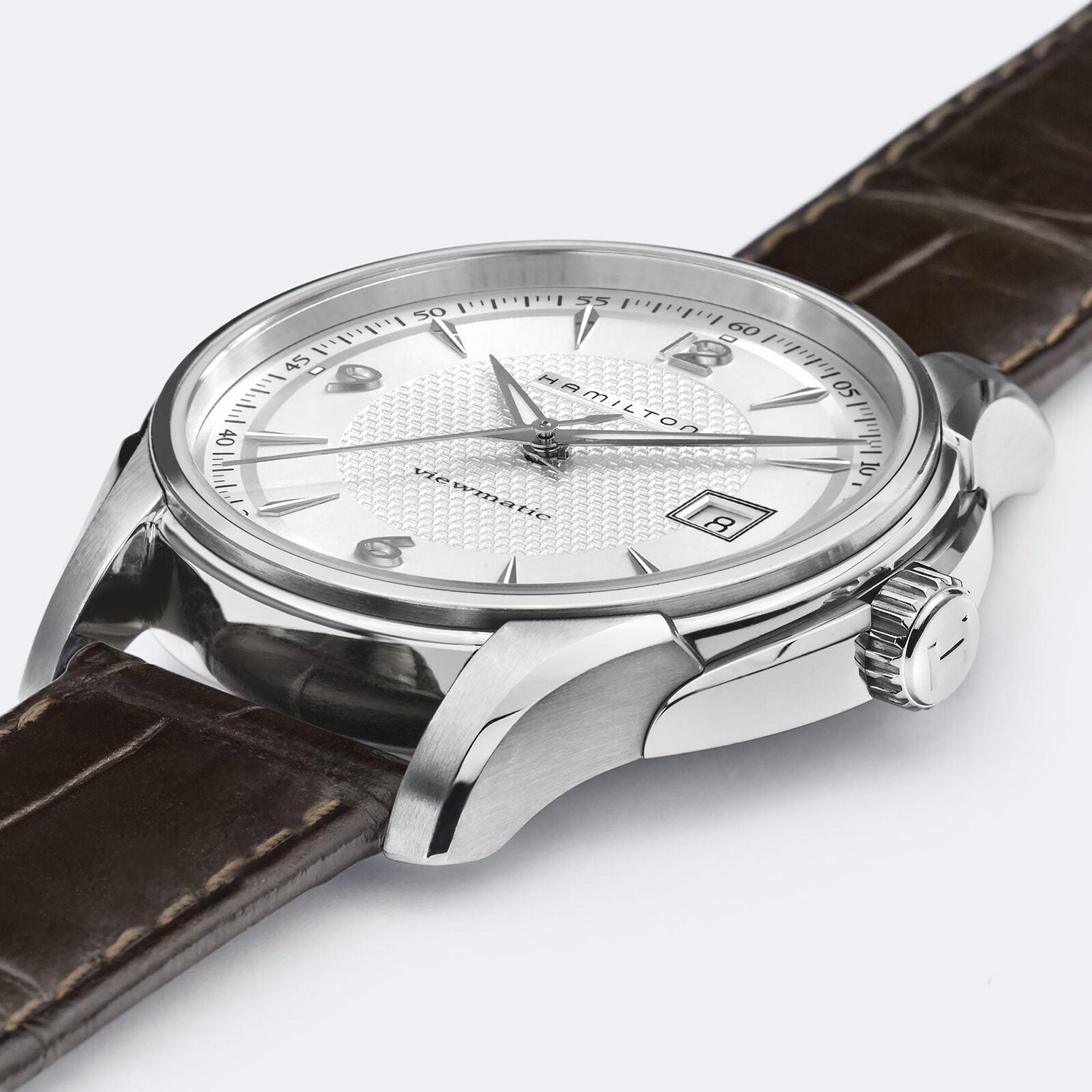 A close-up of the Hamilton Jazzmaster Viewmatic Auto shows its textured white dial, date window at 3 o’clock, silver case, and brown leather strap—showcasing modern craftsmanship from Hamilton.