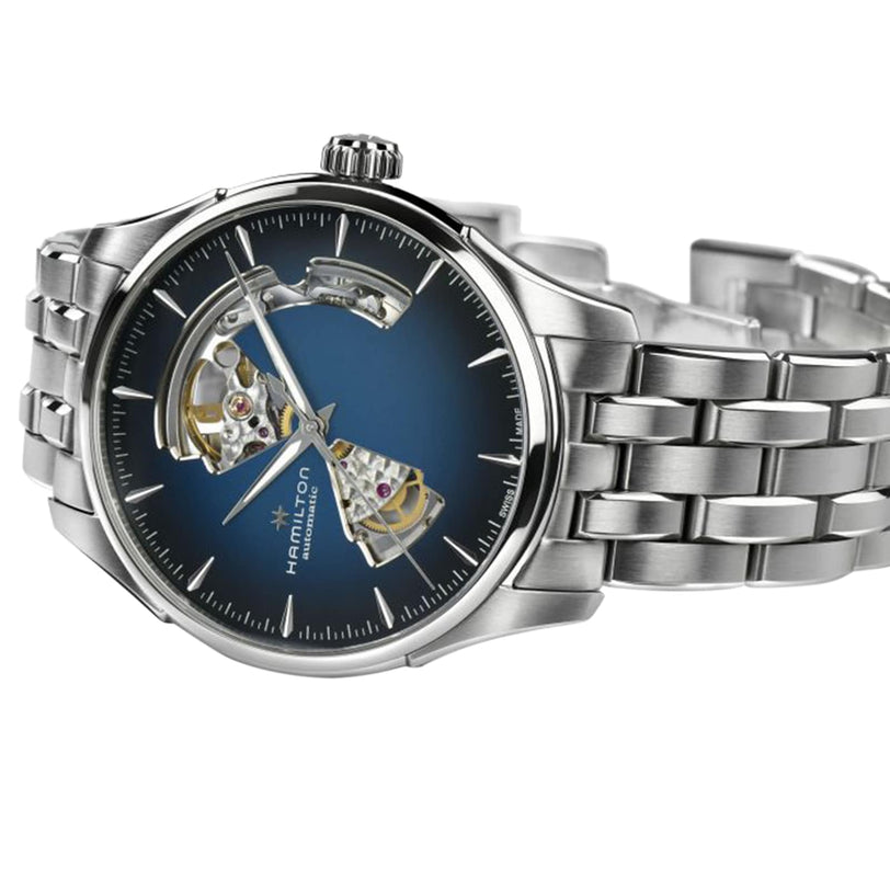 The Hamilton Jazzmaster Open Heart Auto features a silver-tone case, blue smoked partially openwork dial revealing internal gears, and a metal link bracelet, shown on a white background for a modern, stylish presentation.