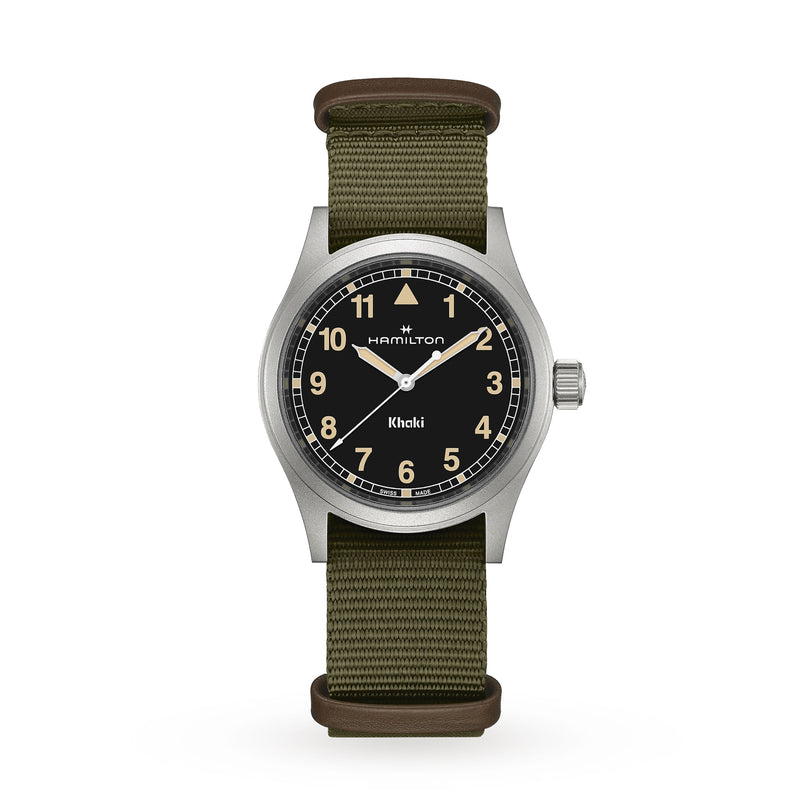 A Hamilton Khaki Field Quartz watch with a black dial and olive green fabric strap is displayed against a white background.