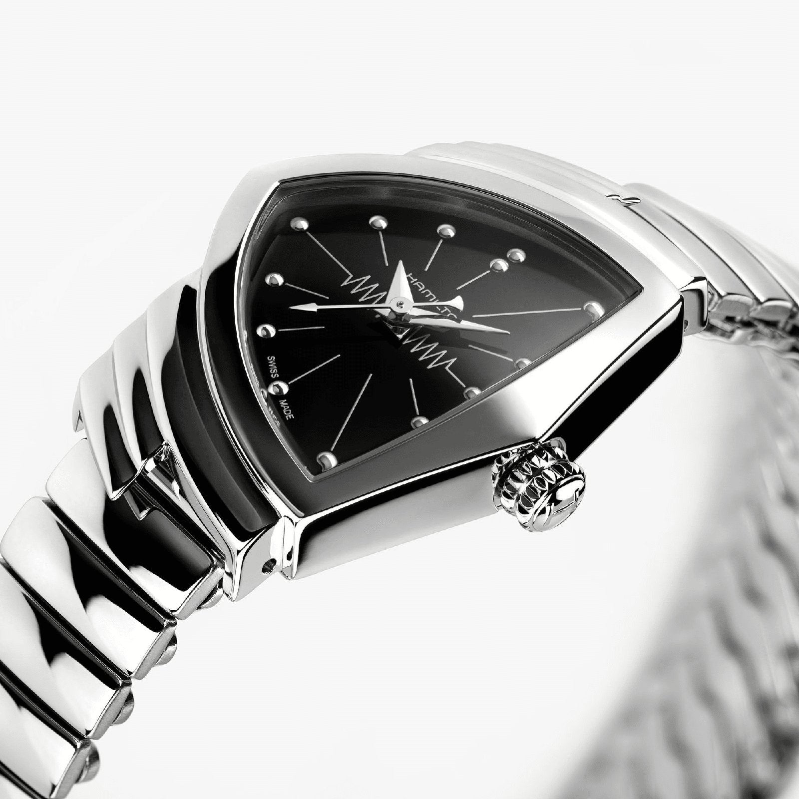 A close-up of the Hamilton Ventura S Quartz shows its silver case, black triangular dial with metallic hour markers, zigzag pattern, and a sleek metal link band inspired by Mid-Century Modern design.