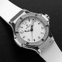 A Hublot Big Bang Steel White Diamonds watch featuring a white dial, stainless steel bezel set with 126 diamonds, and a white strap is showcased on a black textured surface.