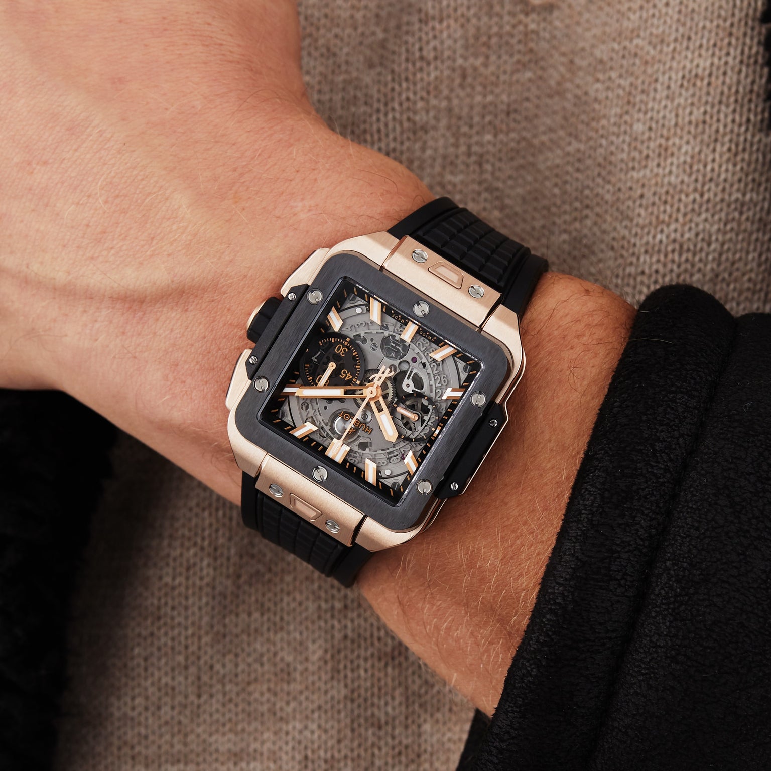 A close-up of a wrist wearing the Hublot Square Bang Unico King Gold Ceramic, featuring an 18K King gold and black case, black rubber strap, and the signature HUB1280 UNICO movement.