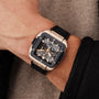 A close-up of a wrist wearing the Hublot Square Bang Unico King Gold Ceramic, featuring an 18K King gold and black case, black rubber strap, and the signature HUB1280 UNICO movement.