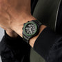 A person wearing a black and green Hublot Big Bang Unico The Watches of Switzerland Group Exclusive with a camo strap, paired with a black jacket and green shirt, highlights the bold style of this limited-edition timepiece.