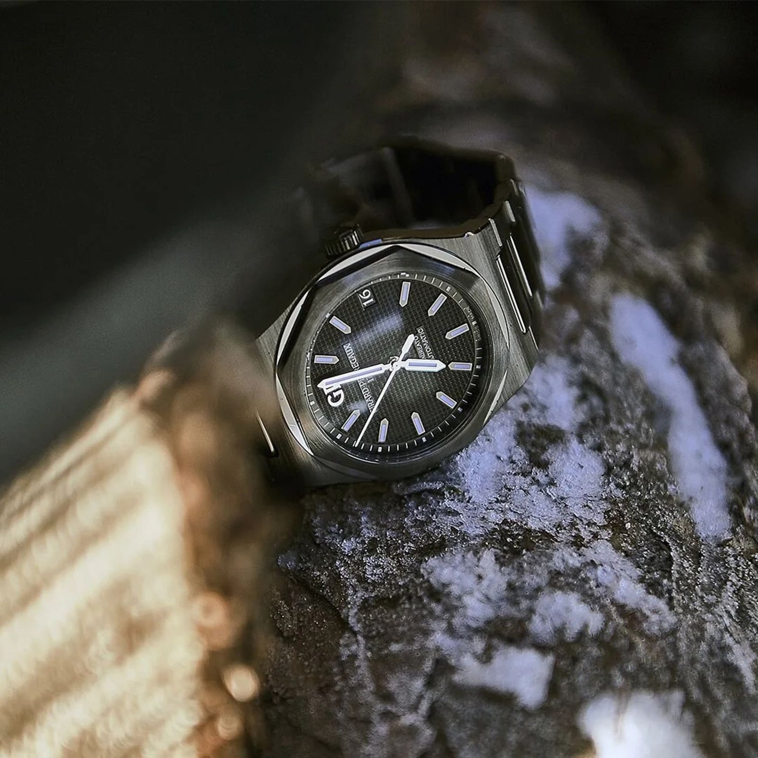 The Girard-Perregaux Laureato 42, featuring a black textured dial and silver octagonal bezel, rests on a rough, snow-dusted tree branch in natural light.