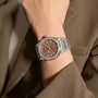 A person in a brown suit jacket wears the Girard-Perregaux Laureato 38, featuring an octagonal diamond-encrusted bezel and a brown patterned dial.