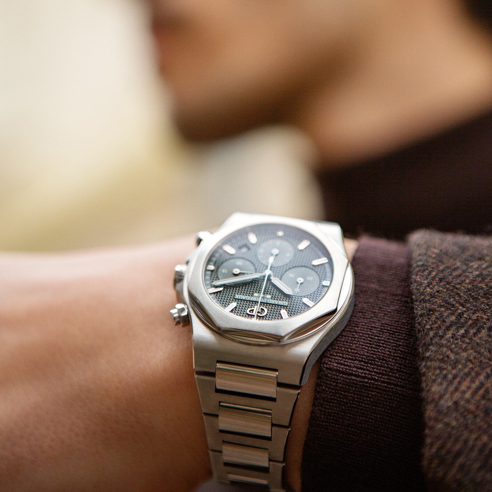 Close-up of the Girard-Perregaux Laureato Chronograph Ti49 in Grade 5 titanium, featuring a dark dial and chronograph functions on a wrist outdoors with a softly blurred background.