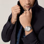 Man adjusting the collar of a dark jacket, wearing a Cartier Ballon Bleu de Cartier watch with a steel case and Roman numerals on his left wrist.