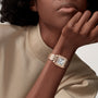 A person in a beige shirt rests their chin on their hand, showcasing the Cartier Panthère de Cartier watch with a square face, Roman numerals, and a blue sapphire crown.