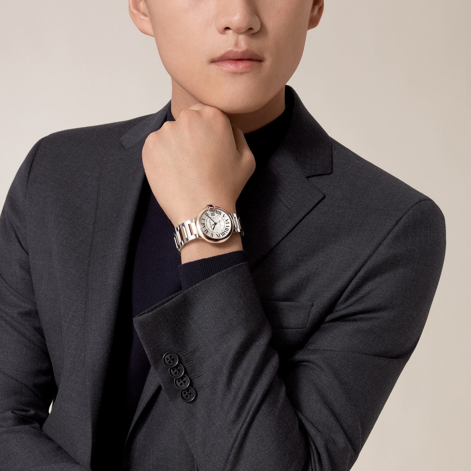 A person in a dark suit poses with their hand under their chin, showcasing the Ballon Bleu de Cartier watch by Cartier, featuring a round face and an elegant interchangeable bracelet.