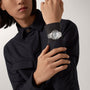 Person in a dark button-up shirt showcases the Cartier Ballon Bleu de Cartier, featuring a round face, Roman numerals, mechanical movement, and a steel interchangeable bracelet on their left wrist.