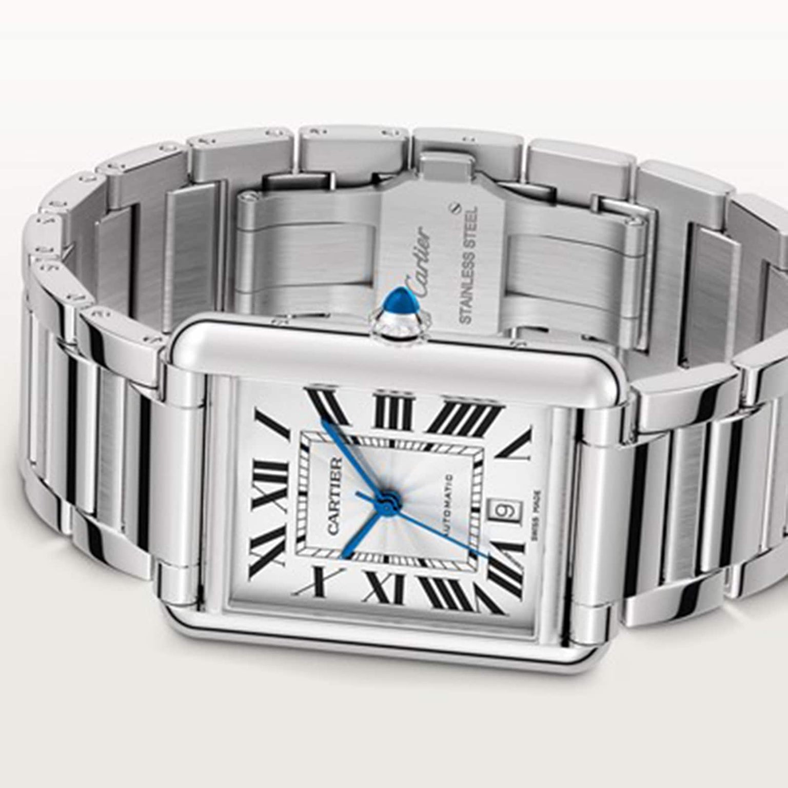 The Cartier Tank Américaine is a stainless steel watch featuring a rectangular silvered flinqué dial with Roman numerals, blue hands, mechanical movement, date window, and an unfastened bracelet.