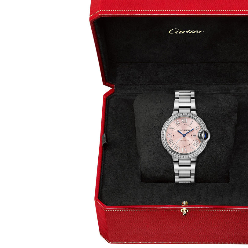The Ballon Bleu de Cartier, a silver watch with a pink sunray dial and Roman numerals, is displayed in an open red and black Cartier box.