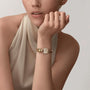 A woman in a sleeveless, light top rests her chin on her hand, showcasing Cartier’s La Panthère de Cartier yellow gold watch featuring panther heads and brilliant-cut diamonds on its decorative band.