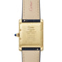 Close-up of the back of a Cartier Tank Américaine wristwatch with a gold Art Deco case featuring engraved markings and a blue gemstone on the crown, paired with beige leather straps.