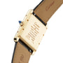 Close-up of the back of a gold Cartier Tank Américaine watch with engraved details like serial numbers and SWISS MADE, paired with a black leather strap—a timeless tribute to Art Deco style.