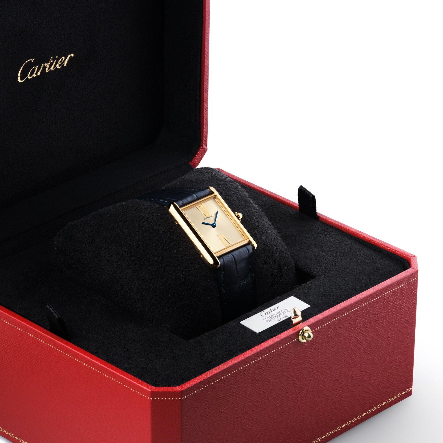 A Cartier Tank Américaine wristwatch with a black leather strap is displayed in an open red Cartier box with black interior, highlighting its enduring Art Deco elegance.