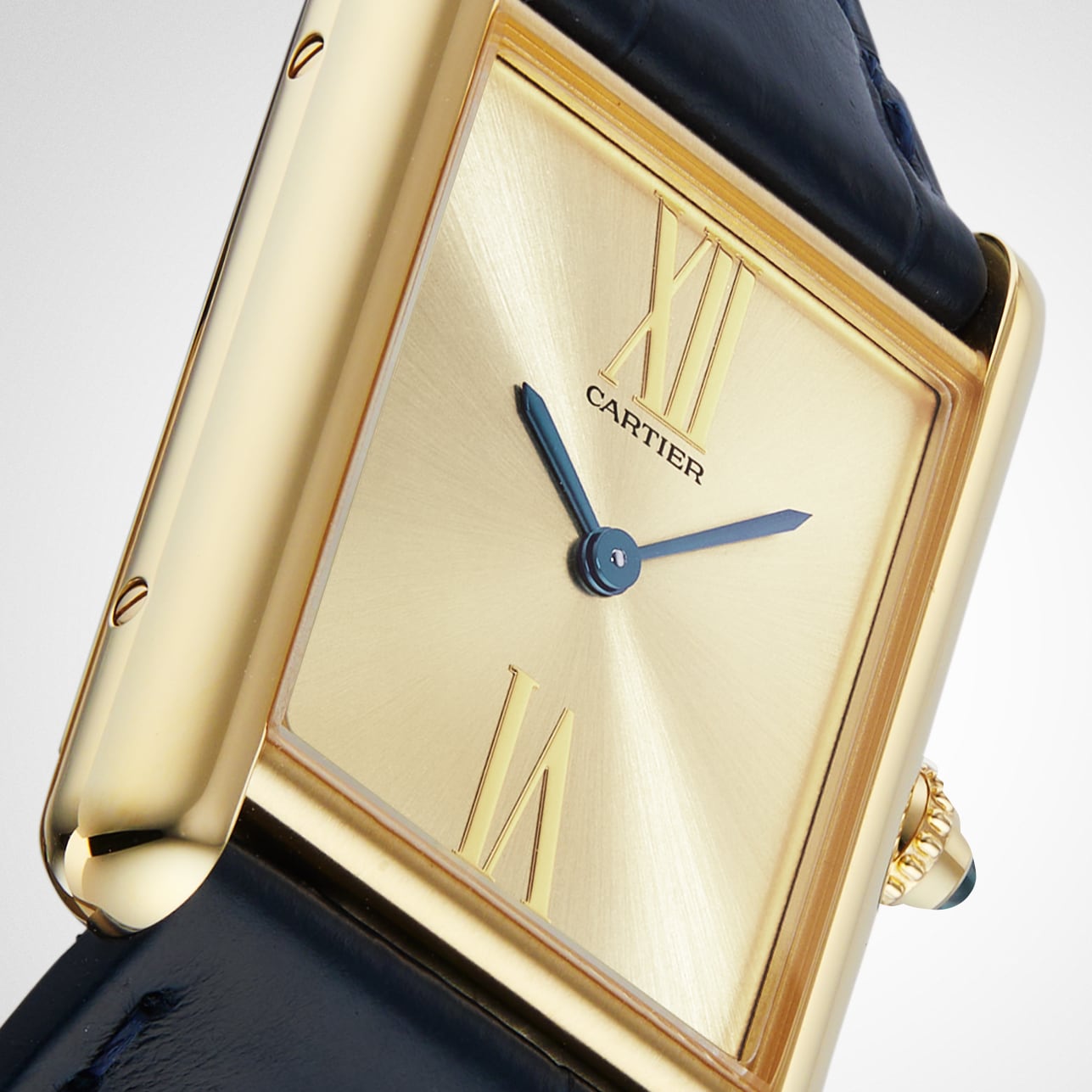 Close-up of a gold Tank Américaine by Cartier featuring a rectangular face, Roman numerals, blue hands, and a black leather strap—a refined Art Deco classic.