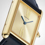 Close-up of a gold Tank Américaine by Cartier featuring a rectangular face, Roman numerals, blue hands, and a black leather strap—a refined Art Deco classic.