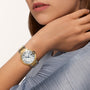 A person wearing a Cartier Ballon Bleu de Cartier wristwatch in 18K yellow gold with a white dial and Roman numerals, dressed in a light blue pleated garment.
