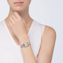 A woman in a sleeveless white top showcases a Cartier Panthère de Cartier Small Model watch with a rectangular face and metal link band, crafted in 18K yellow gold, on her left wrist.