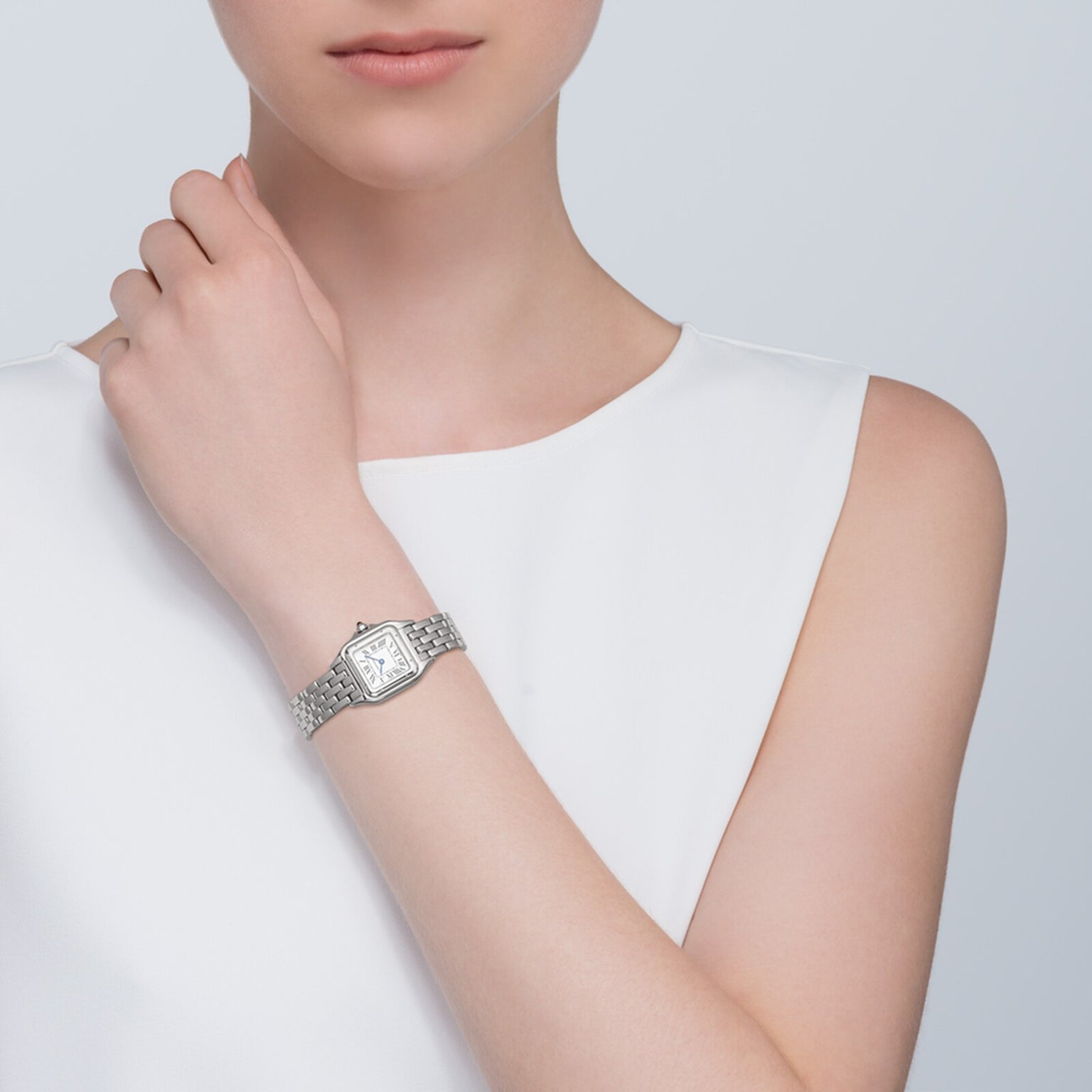 A woman in a white sleeveless top wears the Cartier Panthère de Cartier Small Model silver wristwatch, her hand resting near her collarbone.