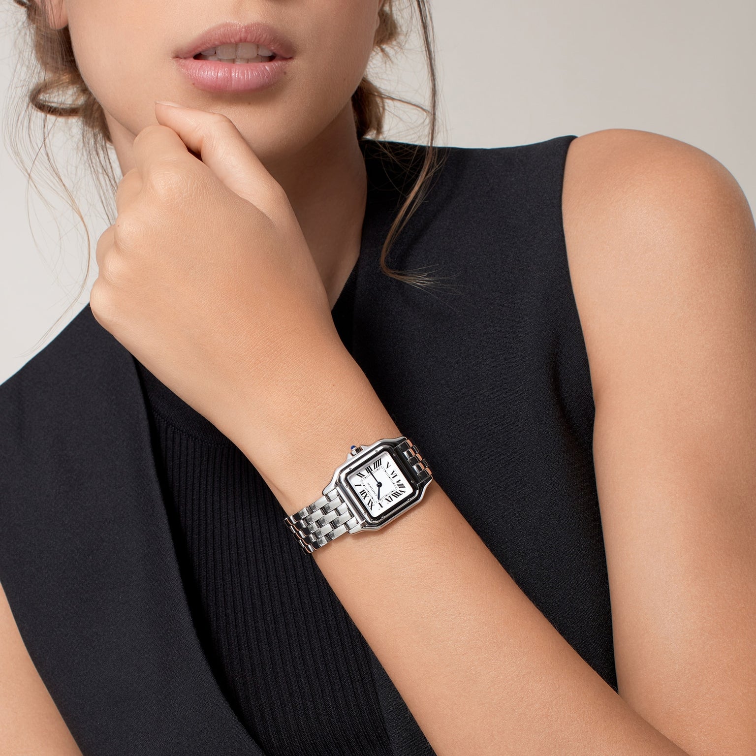 A woman in a sleeveless black top wears the Panthère de Cartier silver wristwatch by Cartier, her hand resting near her chin.