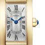 Close-up of the Cartier Tank Américaine watch face with Roman numerals, blue hands, and a gold case featuring a blue gemstone on the crown—a luxurious icon of timeless design.