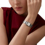 A person in a sleeveless maroon top showcases the Cartier Tank Française watch, featuring a steel case and square face, on their left wrist against a plain background.