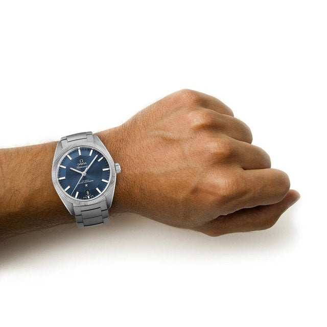 A person’s wrist wearing an OMEGA Constellation Globemaster with a blue dial and stainless steel case, set against a plain white background.