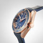 A close-up of the OMEGA Seamaster Planet Ocean 600M, featuring a blue face, blue bezel, gold accents, and a blue leather strap, set against a plain light background.