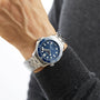 A person wearing an OMEGA Seamaster Diver 300M wristwatch with a blue dial and rotating bezel, dressed in a dark gray long-sleeve shirt.