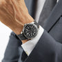 A person in a suit wears an OMEGA Seamaster Diver 300M, featuring a black and silver analog design, rubber strap, and textured black dial.