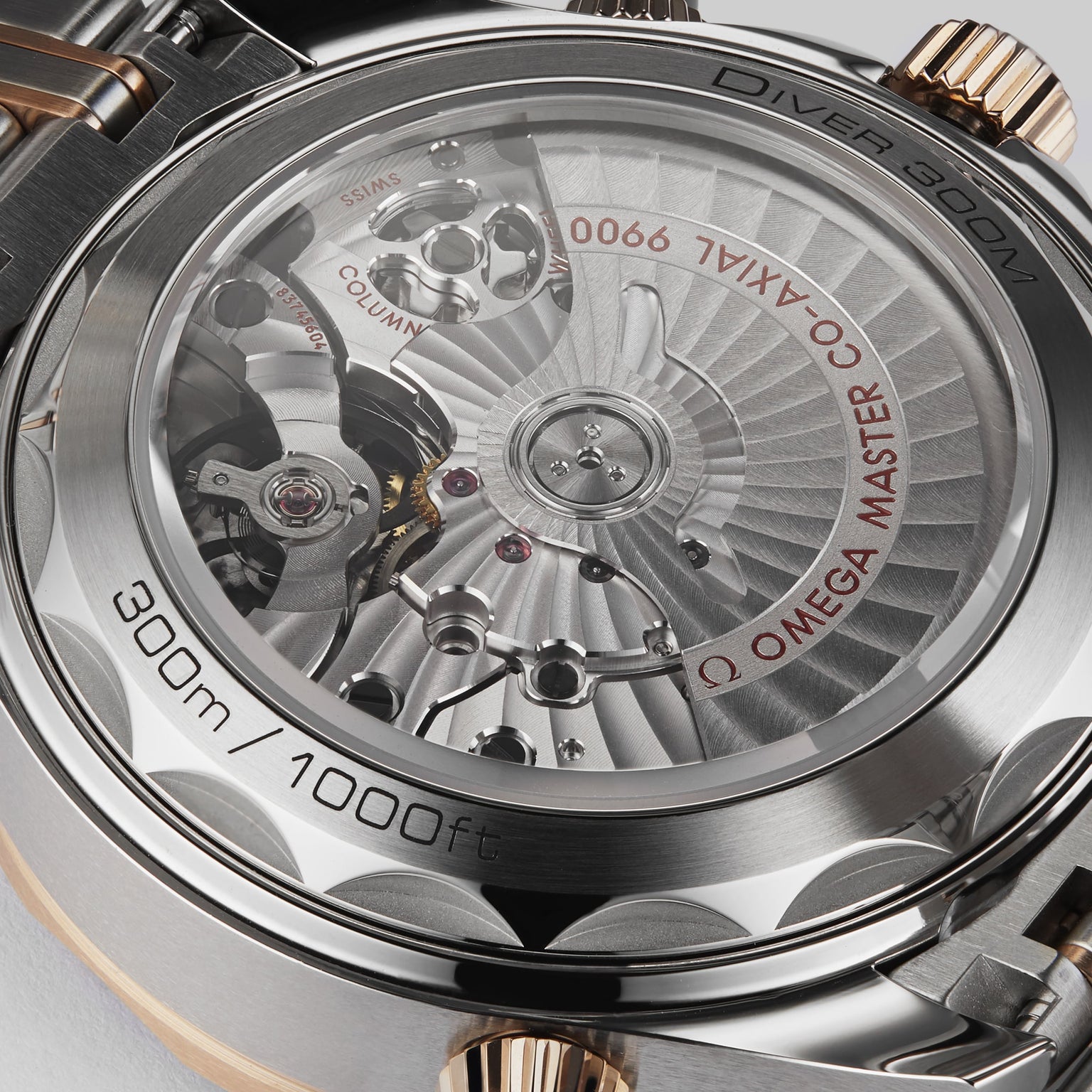Close-up of the OMEGA Seamaster Diver 300M’s back reveals its mechanical movement, rotor, and engravings like 300m/1000ft, Master Chronometer, and Co-Axial 9900 in luxurious 18K Sedna™ gold.